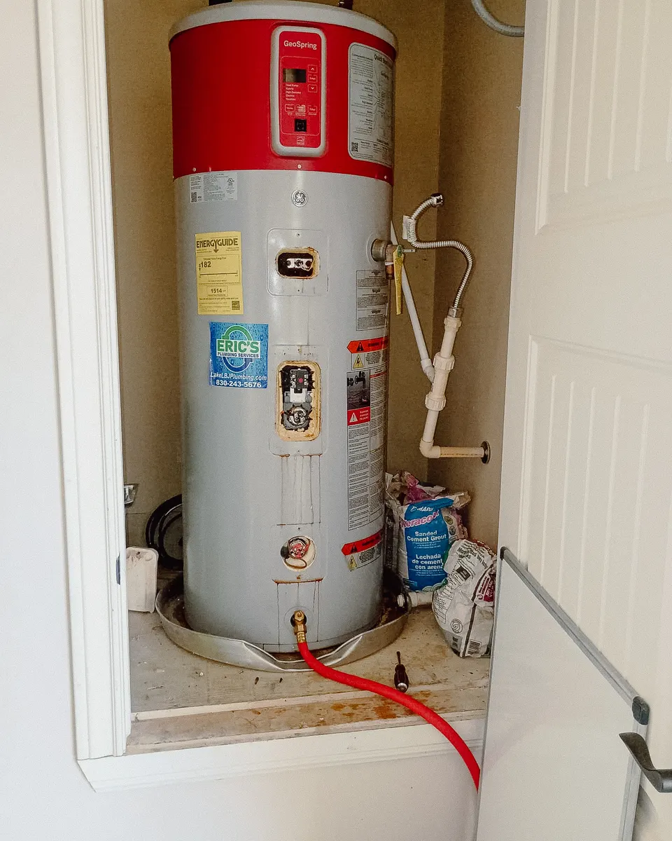 Old heat pump water heater being drained in a utility closet
