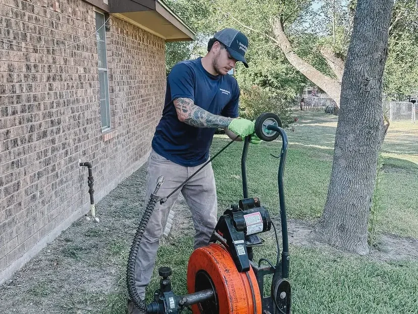 Brandenburg plumber running a drain machine outside a brick home